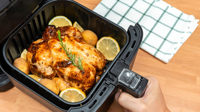 whole chicken in an air fryer with herbs, lemon slices and potatoes
