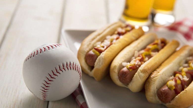 Three hot dogs next to a baseball.