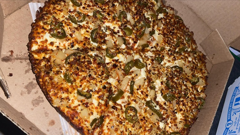 A crispy pan crust pizza with peppers and pineaple on it in a box from Domino's