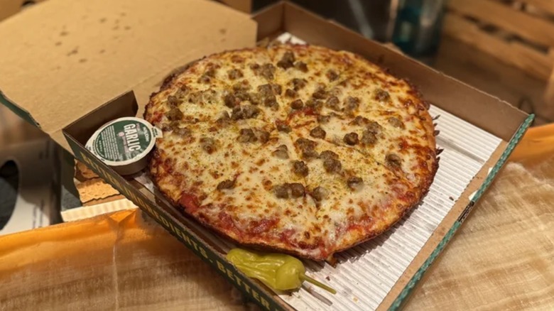 A sausage and cheese pan pizza from Papa John's in its pizza box beside a pepper and some garlic sauce.