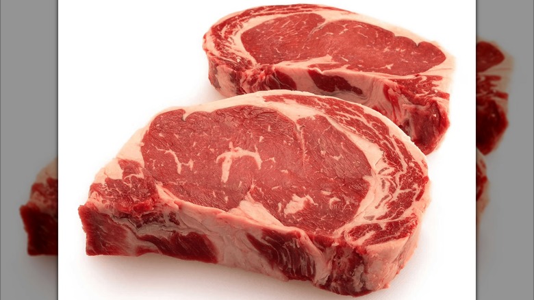 Two boneless, raw ribeye steaks with strong marbling sitting on a white surface.