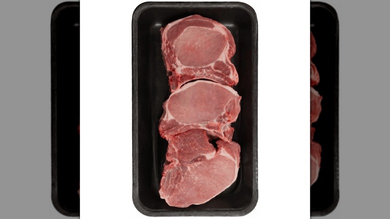 Three raw bone-in pork chops in black Styrofoam on a white background.