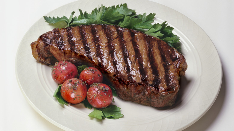 New York strip steak on a white plate with flat-leaf parsley and cherry tomatoes