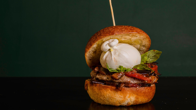 A burger topped with burrata cheese, basil, and grilled tomato with a toothpick sticking out the top