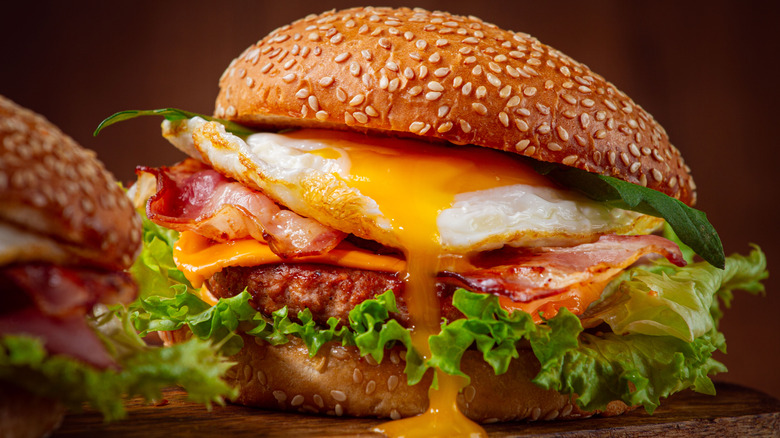 A burger with a fried egg, cheese, bacon, and lettuce on a sesame seed bun