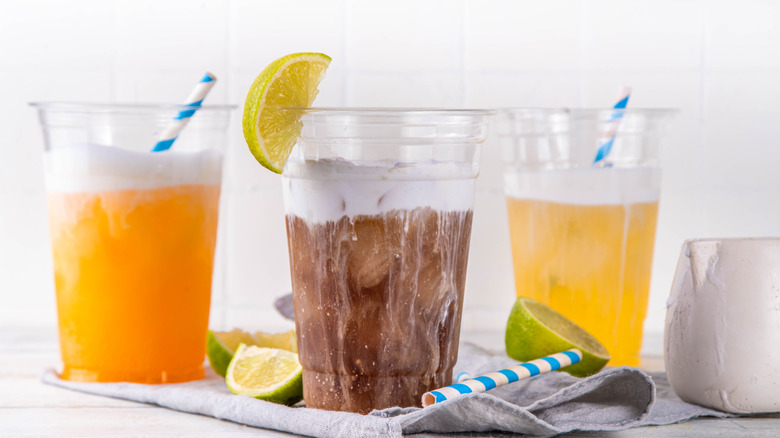 Three dirty sodas with white cream tops in clear plastic cups