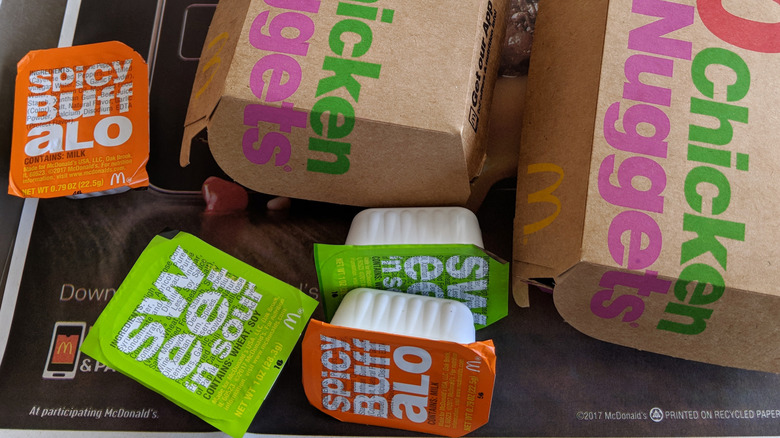 Several pots of unopened McDonald's dipping sauces on a tray with boxes of chicken nuggets