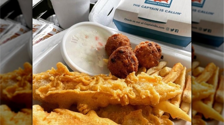 A close image of battered fish, fries, coleslaw, and hush puppies in a takeout container from Captain D's.