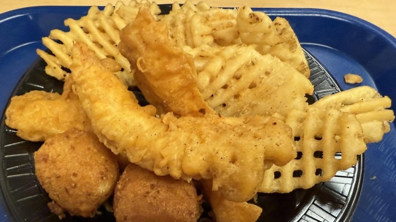 A black plastic plate on a dark blue plastic tray, filled with fried fish, hush puppies, and waffle fries from Long John Silver's.