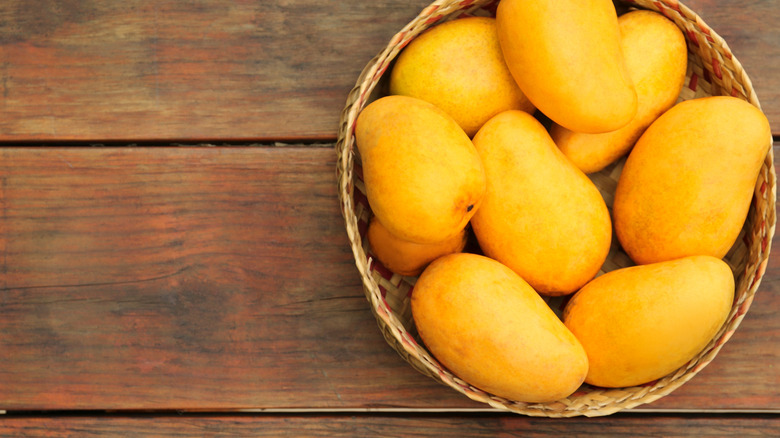 A bowl of yellow Ataulfo mangoes on a wooden table seen from above