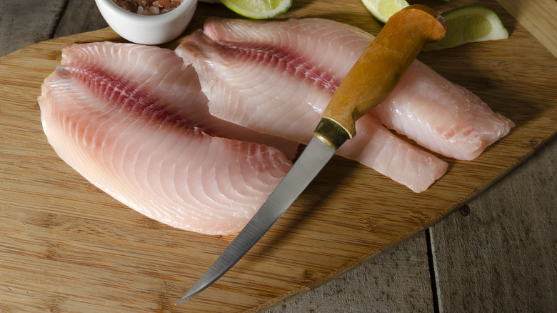 Tilapia fillets with a boning or fillet knife placed on top of them.