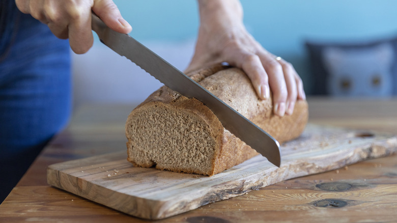 A person using a bread knife to slice bread.