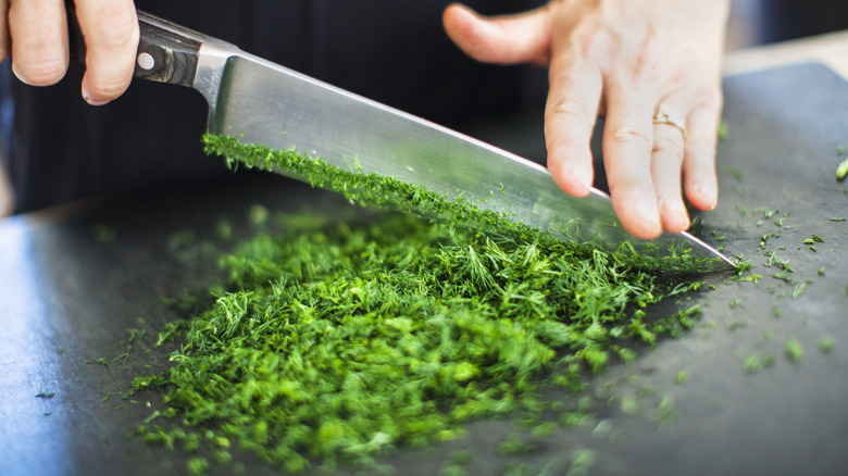 A person using chef's knife to chop parsley.