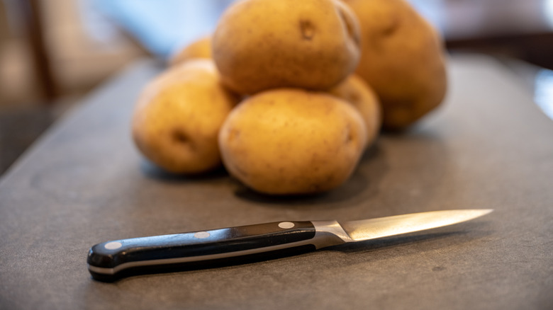 A pile of potatoes sitting beside a paring knife.