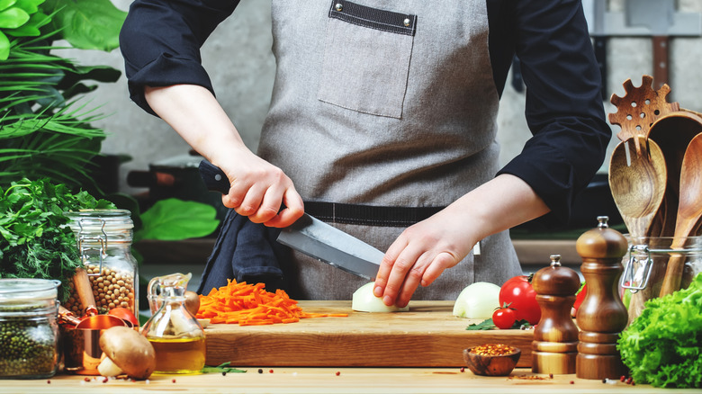 A person using a santoku knife to chop an onion.