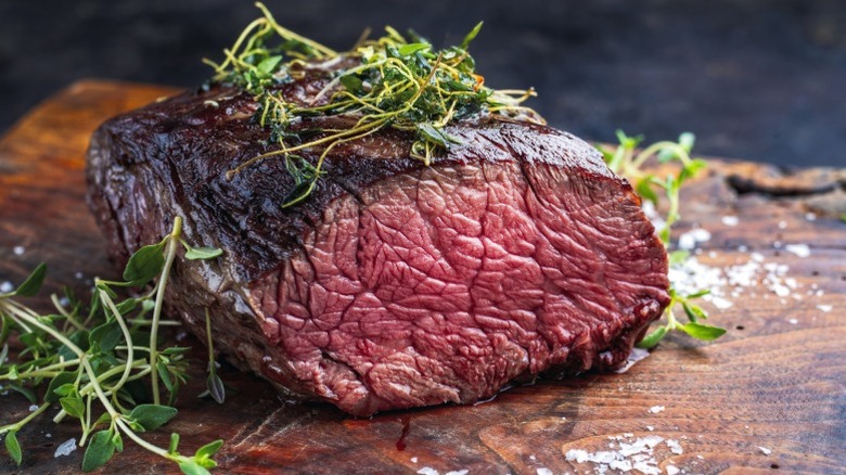 A piece of chuck eye roast cooked medium sitting on a wood board with garnishes.