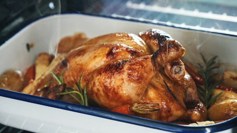 A roast chicken in a roasting pan with vegetables and herbs.