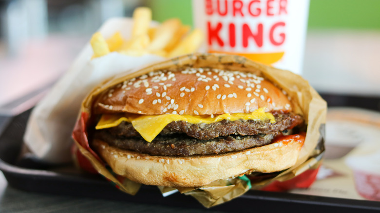 A double burger from Burger King with a drink in the background