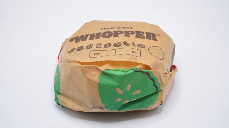 A Burger King Whopper in its packaging on a grey background.