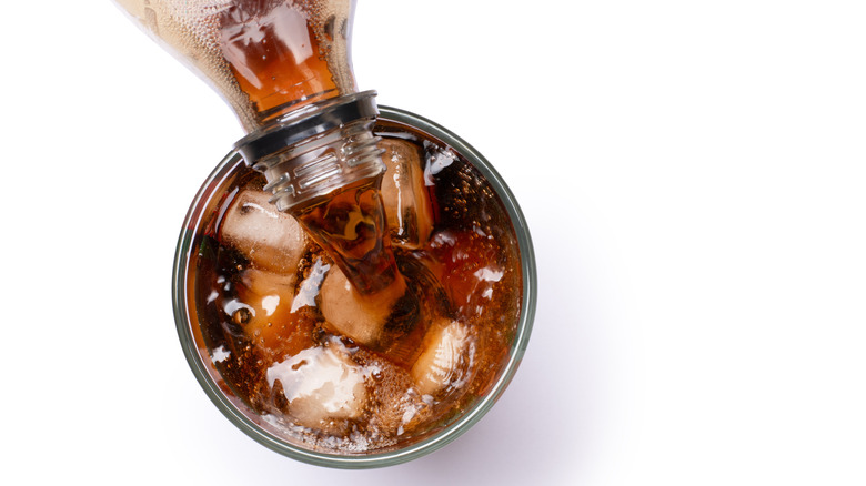 A glass of coke with ice being poured from a bottle, shot from above