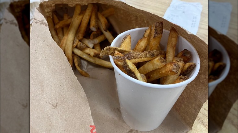 An order of French fries from Five Guys in a white cup and in the bag