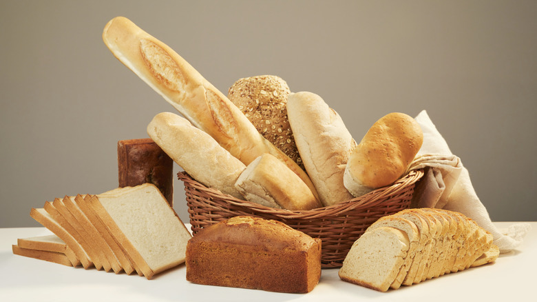 Various loaves of bread in and around a basket on a white surface