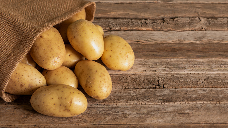 potatoes spilling from a sack onto a wooden surface