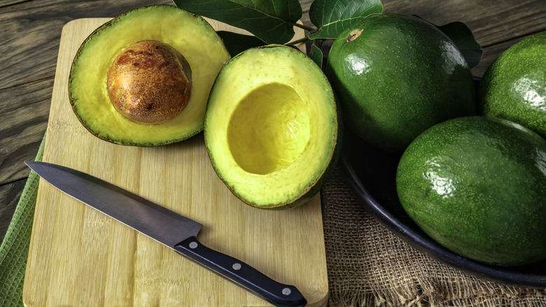 Avocados in a bowl alongside a halved avocado on a cutting board