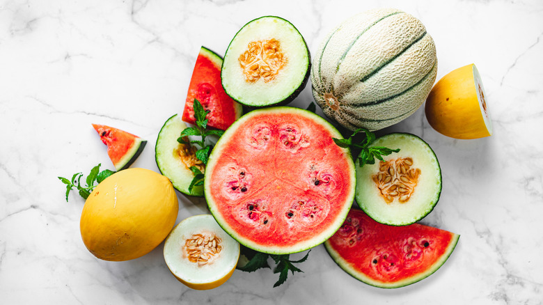 Top view of various whole and halved melons on a marble countertop