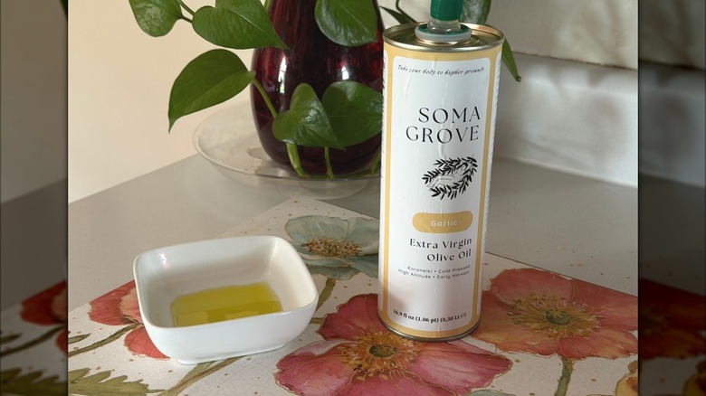 A metal bottle of Soma Grove garlic-infused olive oil next to a small bowl filled with oil.