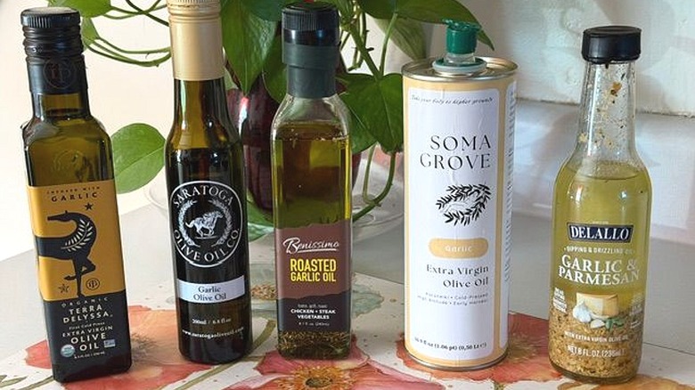 Five small bottles of garlic-infused olive oil on kitchen table, including brands like Terra Delyssa and Saratoga