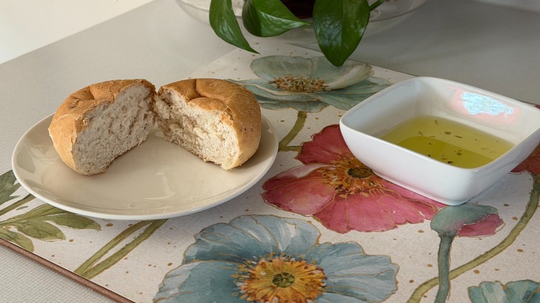 A small plate with a dinner roll cut in two next to a small bowl of olive oil.