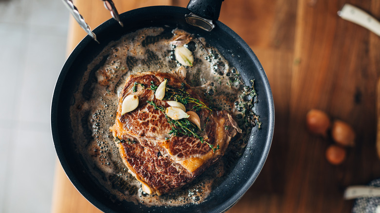Ribeye steak pan frying in butter, garlic, and herbs.
