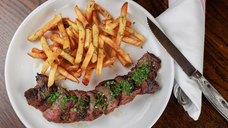 Steak and fries on white plate with knife