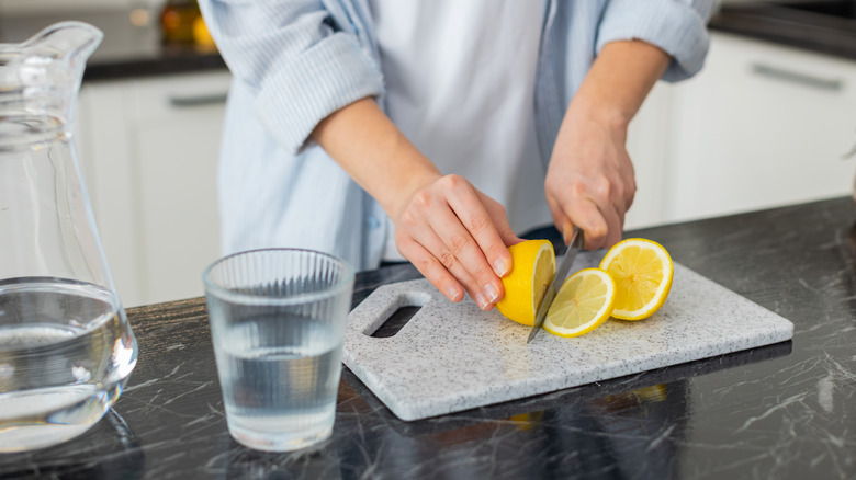 Person slicing a lemon near a glass and pitcher of water