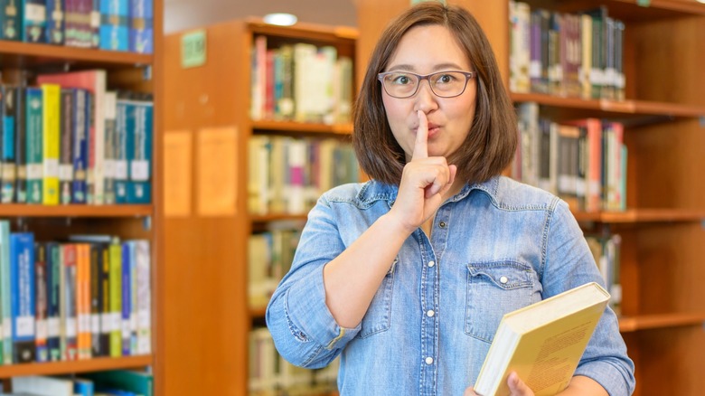 Woman holding book shushing with her finger in the library.