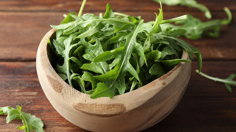 Fresh green arugula leaves in a bowl on a wooden table.