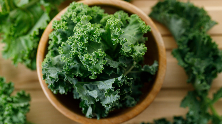 Fresh green kale leaf salad vegetable in wooden bowl on wooden background.
