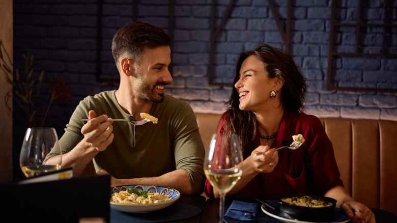 A couple sitting at a restaurant smiling and eating food.