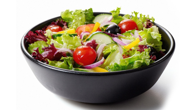A garden-style salad in a black bowl on a white background.