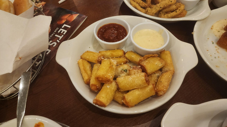 Olive Ziti Fritta on a hot plate with two dipping sauces surrounded by other appetizers.
