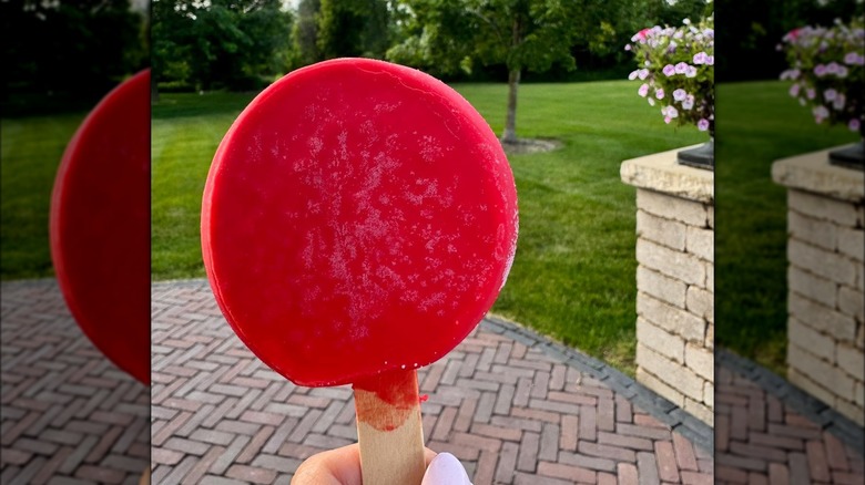 Person holding cherry Dilly Bar with grass yard in background