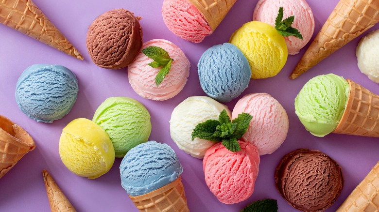 Scoops of ice cream in various colors and cones scattered on a purple surface