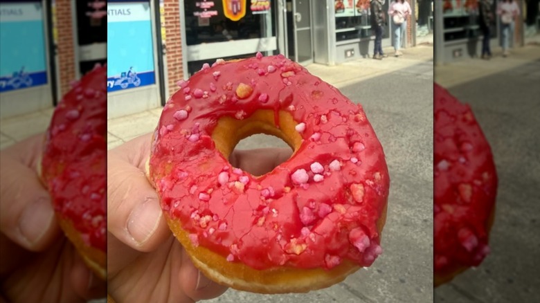 Someone holding a Fruit Punch Donut from Dunkin' in their hand outside.