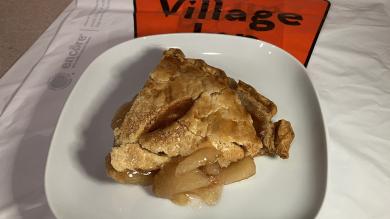 A slice of apple pie on a white plate on top of a Village Inn Restaurant takeout bag
