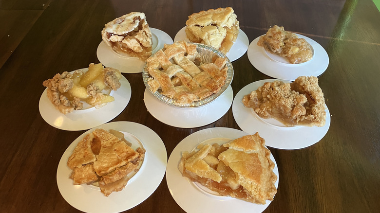 Eight apple pies displayed on round white plates in a circle on a dark wood table