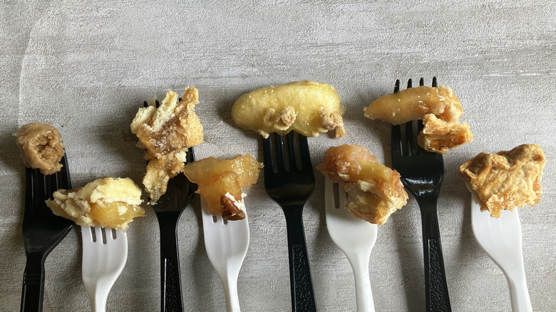 Eight forks in alternating black and white colors balance small bites of various apple pies