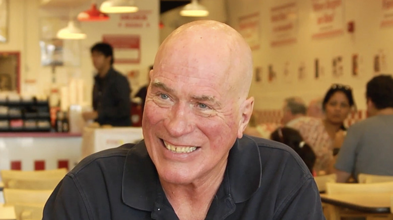 Jerry Murrell, Founder and CEO of Five Guys, smiling during an interview in a Five Guys restaurant.