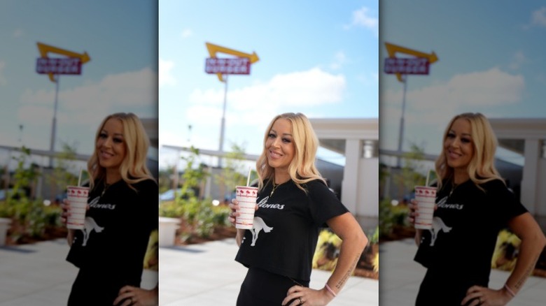 A photo of In-N-Out President Lynsi Snyder in front of a restaurant sign with drink in hand.