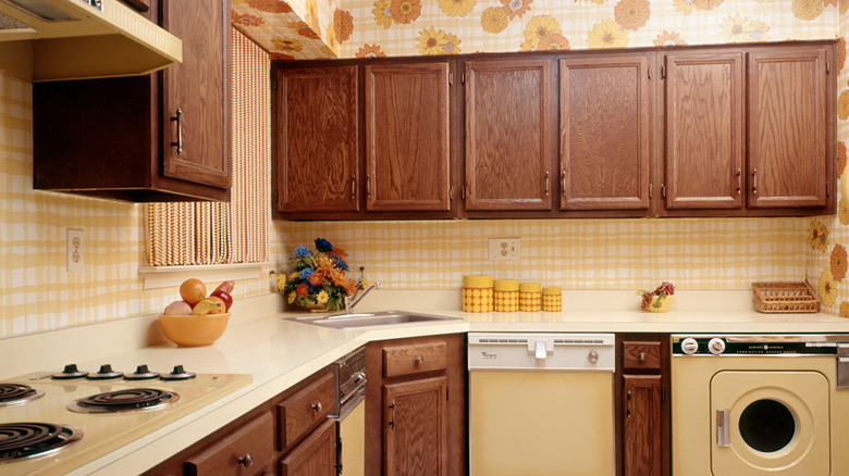 A kitchen from the 1970s complete with wood cabinetry and flower wallpaper.